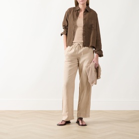 Model wearing Marc O Polo Solid Logo Tank Top in Sandpaper, styled with brown overshirt, beige linen trousers and brown flat sandals.