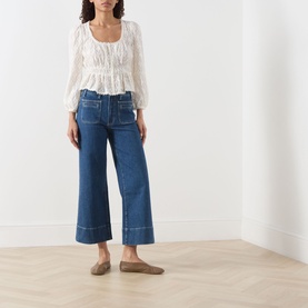 Model wearing Paige Jay Embroidered Blouse in Antique White with square neckline and ruffled hem, styled with wide-leg blue jeans and taupe flats.