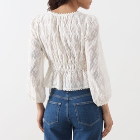 Model wearing Paige Jay Embroidered Blouse in Antique White with elasticated waist and ruffled hem, styled with blue denim jeans. Back view.