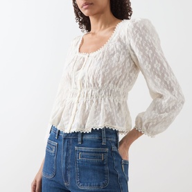 Model wearing Paige Jay Embroidered Blouse in Antique White with square neckline, elasticated waist and ruffled hem, styled with blue jeans.