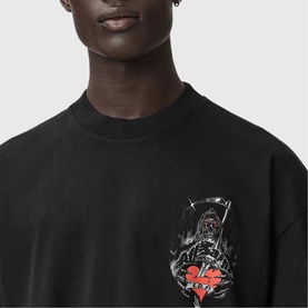 Model wearing All Saints washed black oversized T-shirt with gothic reaper and heart graphic print on chest