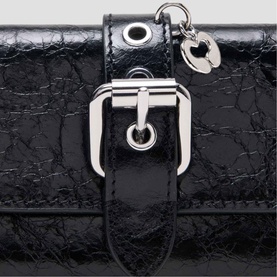 Maje red crinkled patent leather bag close-up with silver buckle hardware, eyelet detail, and heart charm