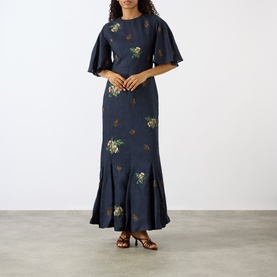 Model wearing Agua Bendita Ave Anhelo Dress in navy with multicolour floral embroidery, flutter sleeves, fitted waist and flared maxi hem