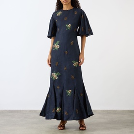 Model wearing Agua Bendita Ave Anhelo Dress in navy with multicolour floral embroidery, flowy short sleeves, fitted waist and flared maxi hem.