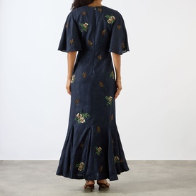 Model wearing Agua Bendita Ave Anhelo Dress in navy with multicolour hand-embroidered floral detailing, short flutter sleeves, and flared maxi hem,