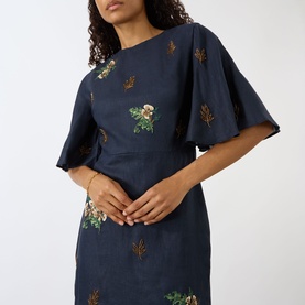 Model wearing Agua Bendita Ave Anhelo Dress in navy with multicolour hand-embroidered floral detailing, round neckline and short flowy sleeves