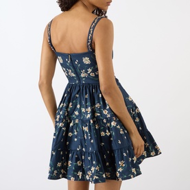 Model wearing Agua Bendita Lima Promesa Mini Dress in multicolour navy floral print, showing back view with fitted waist, tiered A-line skirt and