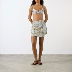 Model wearing Agua Bendita Luna Valle Mini Skirt in multicolour floral print with wrap silhouette and scalloped hem, styled with matching bikini top