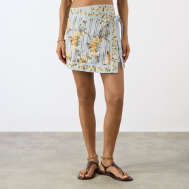 Model wearing Agua Bendita Luna Valle Mini Skirt in multicolour floral stripe print with tie waist, styled with tan flat sandals.