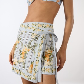 Model wearing Agua Bendita Luna Valle Mini Skirt in multicolour floral stripe print with tie waist and scalloped hem, styled with matching crop top.