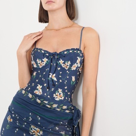 Model wearing Agua Bendita multicolour floral swimsuit with tie-front bust and ruched skirt overlay, styled with a gold chain necklace.