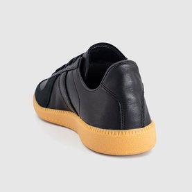 Adidas trainer in core black leather with three-stripe detail and contrasting gum rubber sole, rear angle view