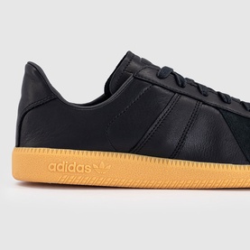 Adidas trainer in core black leather with three-stripe detail and contrasting gum rubber sole, close-up angle.