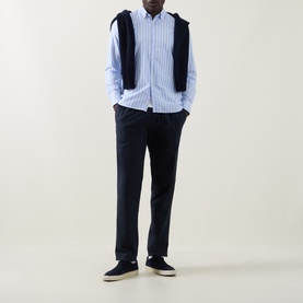 Model wearing Bugatti Soft Oxford Shirt in blue stripe with navy sweater vest, navy trousers and dark canvas trainers.