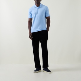 Model wearing Bugatti light blue polo shirt with navy trousers and navy canvas trainers with white soles.