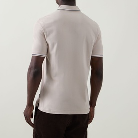 Model wearing Bugatti beige cotton polo shirt, rear view, with white tipped collar and sleeve edges, styled with dark trousers.