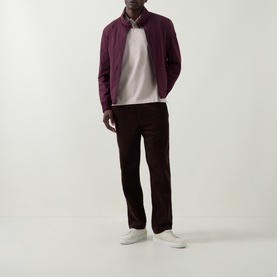 Model wearing Bugatti beige cotton polo, styled with a burgundy zip-up jacket, dark trousers, and white trainers.