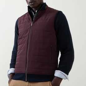 Model wearing Bugatti blackberry quilted gilet layered over navy knit sweater and striped shirt.