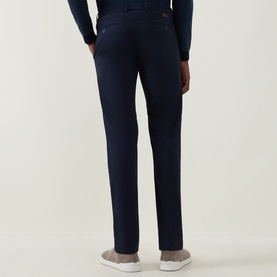 Model wearing Bugatti Lux Slim-Leg Chinos in navy, slim fit with clean hems, styled with grey trainers and navy top, rear view.