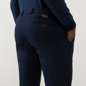 Model wearing Bugatti Lux Slim-Leg Chinos in navy, showing rear jetted pockets with button closures and slim-leg fit, styled with navy knitwear.