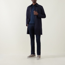 Model wearing Bugatti Lux Slim-Leg Chinos in navy, styled with a navy mac coat, polo shirt, and grey suede trainers.