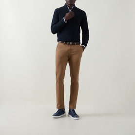 Model wearing Bugatti brass trousers styled with a navy knit jumper, brown belt, and navy trainers.