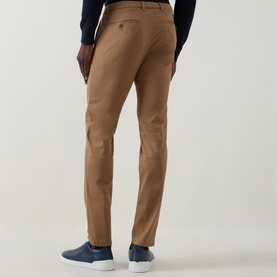 Model wearing Bugatti brass slim-fit chinos, styled with a navy jumper and blue trainers, rear view showing clean tailored finish.