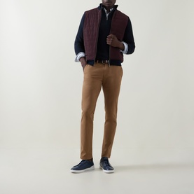 Model wearing Bugatti brass trousers styled with a burgundy quilted gilet, navy jumper, and navy suede trainers.