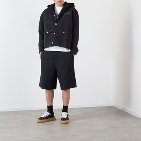 Model wearing black hooded jacket and matching shorts, styled with a white tee, black socks, and black trainers with gum soles