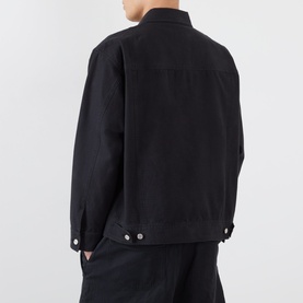Model wearing a black denim jacket, rear view, with silver button cuffs and structured boxy fit