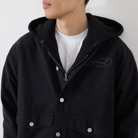 Model wearing black hooded jacket with embroidered chest detail and zip fastening, styled with white T-shirt and gold pendant necklace