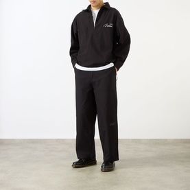 Model wearing Emporium Logo Pullover Polo Shirt in black cotton ripstop, styled with wide-leg black trousers and dark loafers.