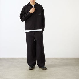 Model wearing Emporium Logo Pullover Polo Shirt in black with wide-leg black trousers and black loafers.