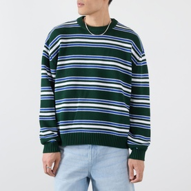 Model wearing Emporium Stripe Fisherman Knit Sweater in green, heavyweight crew neck with multicolour stripes, styled with light blue jeans.