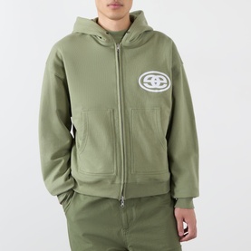 Model wearing Emporium Thermal Logo Hoodie in khaki, zip-through style with embroidered oval logo, styled with matching khaki joggers.