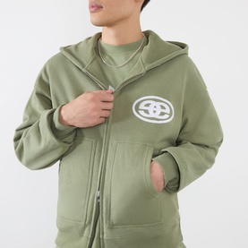 Model wearing Emporium Thermal Logo Hoodie in khaki, zip-up style with embroidered logo patch, over matching khaki sweatshirt.