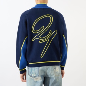 Model wearing Emporium Boca Logo Knitted Zip Sweater in navy, showing back with yellow jacquard logo detail, styled with light wash jeans.
