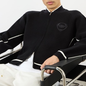 Model wearing Emporium Boca Logo Knitted Zip Sweater in black with white trim, bomber collar, and embroidered chest logo.