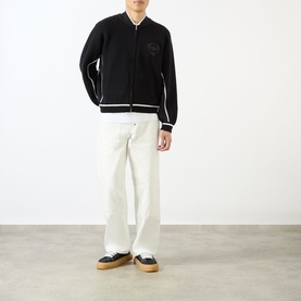 Model wearing Emporium Boca Logo Knitted Zip Sweater in black with white tipping, styled with white straight-leg trousers and gum-sole trainers.