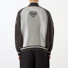 Model wearing Emporium E90 Logo Knitted Zip Sweater in grey, rear view showing jacquard knit pattern and embroidered shield logo.