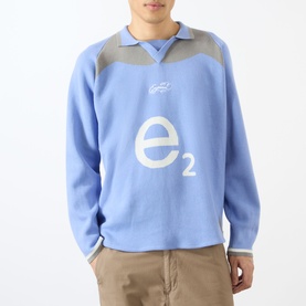 Model wearing Emporium Henry Logo Knitted Sweater in baby blue with jacquard e2 front logo, open polo collar, styled with beige trousers.