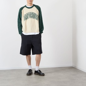 Model wearing Emporium Double-Pocket Shorts in black, styled with a cream and green raglan sweatshirt and black loafers.
