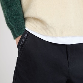 Model wearing Emporium Double-Pocket Shorts in black with tonal branding tab, styled with cream knit and white layer.
