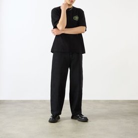Model wearing Emporium black cotton T-shirt with green graphic, styled with wide-leg black trousers and black leather shoes.