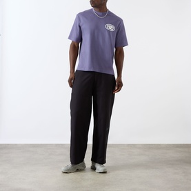 Model wearing Emporium burgundy cotton T-shirt with chest logo graphic, styled with black trousers and grey trainers.