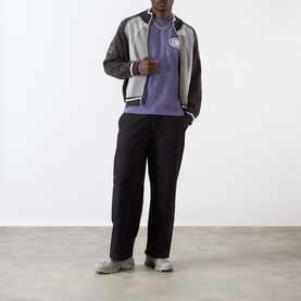Model wearing Emporium burgundy cotton T-shirt, styled with a two-tone varsity jacket and black wide-leg trousers