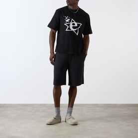 Model wearing Emporium Lucky Stars Logo T-Shirt in black with matching black shorts, grey socks and beige trainers.