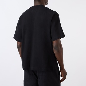 Model wearing Emporium Lucky Stars Logo T-Shirt in black, boxy fit, short sleeves, shown from the back, styled with black trousers.