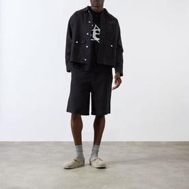 Model wearing Emporium Lucky Stars Logo T-Shirt in black, styled with matching black jacket and shorts, grey socks and beige shoes.