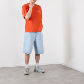 Model wearing Emporium Script Logo T-Shirt in orange with light-wash denim shorts and grey trainers.